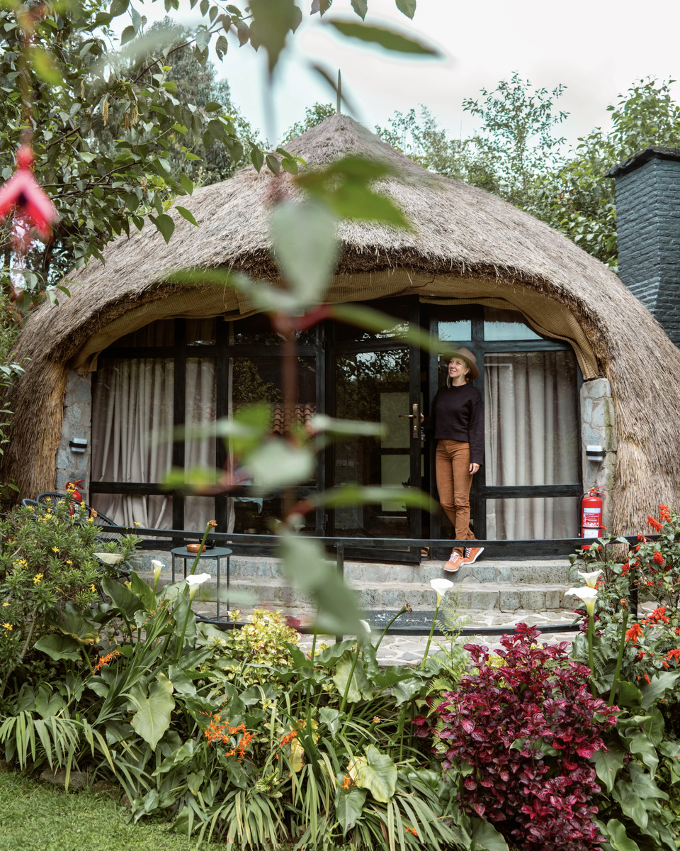 Olga stands in the doorway of a flower-ringed thatched cottage at Amarembo.