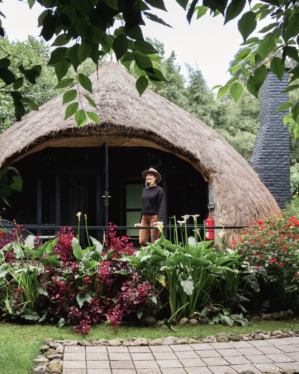 Olga stands on the small terrace of a round cottage beneath its deep thatched roof.