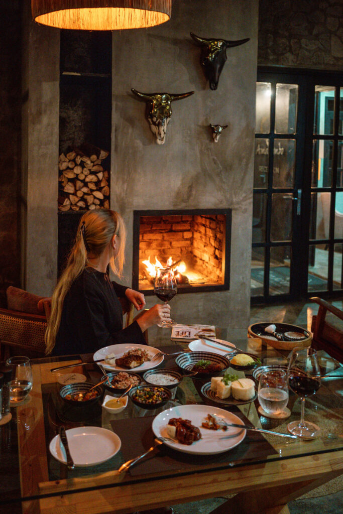 Olga sits at a dinner table set beside a lit fireplace at Amarembo.