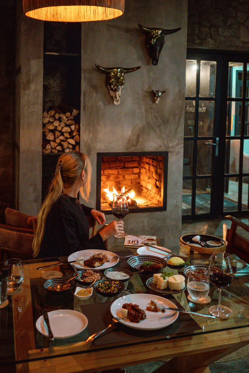 Olga sits at a dinner table set beside a lit fireplace at Amarembo.