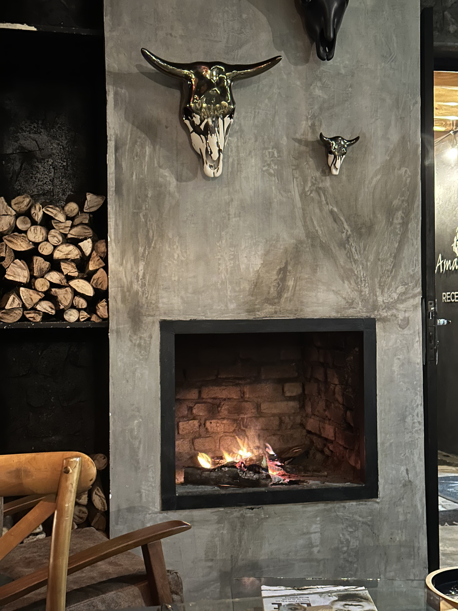 A close view of the Amarembo fireplace shows stacked logs and a gold-and-black animal sculpture above the flames.
