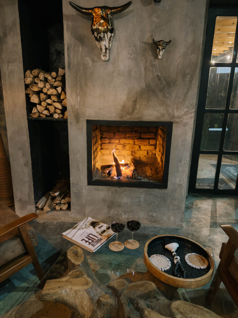 A modern fireplace, stacked logs and sculptural objects form the centre of an Amarembo sitting room.
