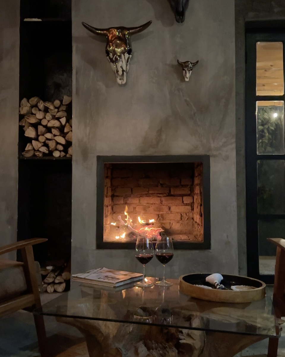 Two glasses of red wine stand on a low table in front of the Amarembo fireplace.