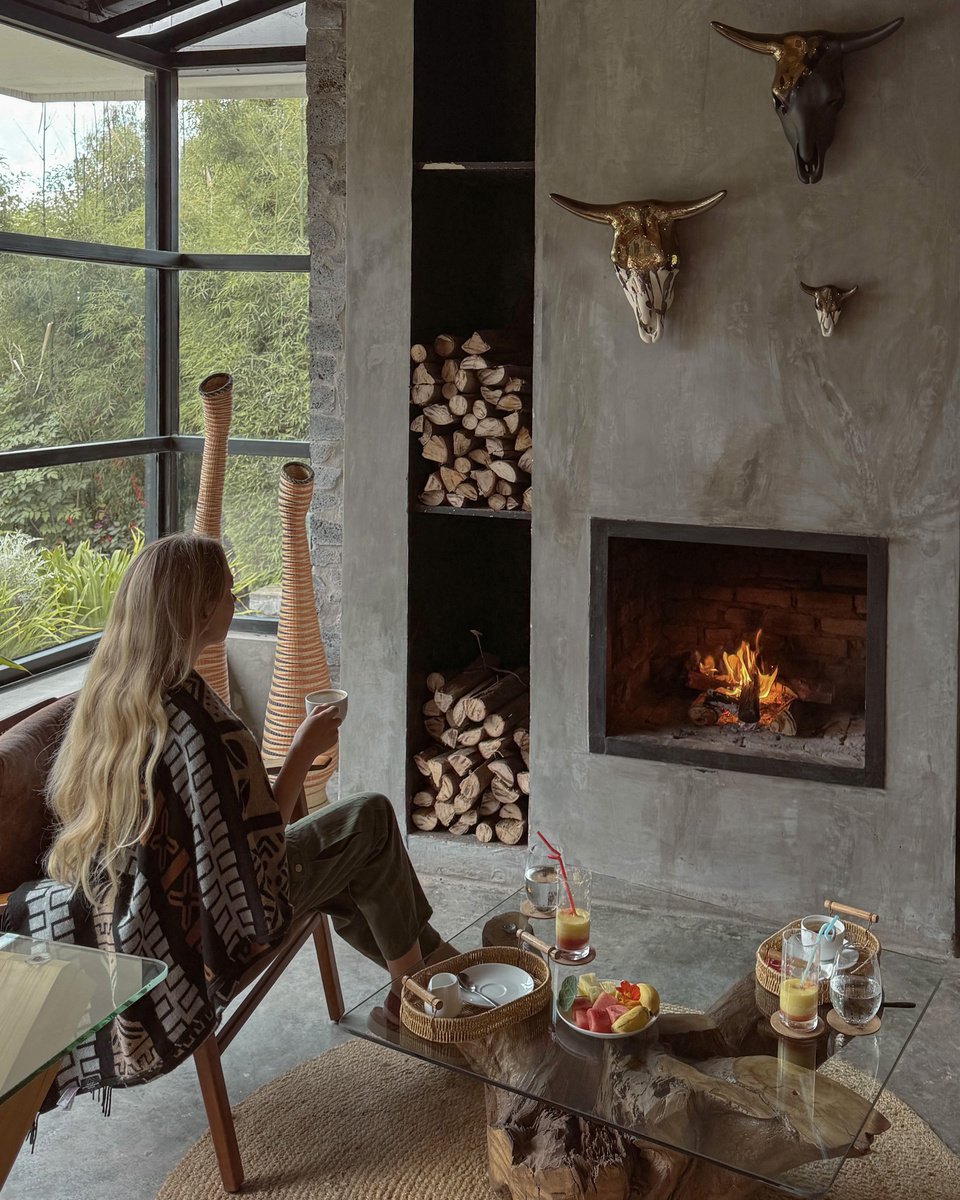 Olga sits by the fireplace with dinner dishes and a glass of wine on the low table.