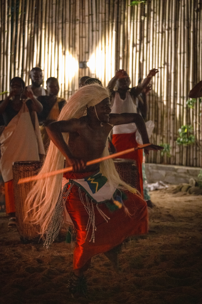 A Gorilla Guardians performer dances in a raffia headdress inside a bamboo-walled hall near Volcanoes National Park.
