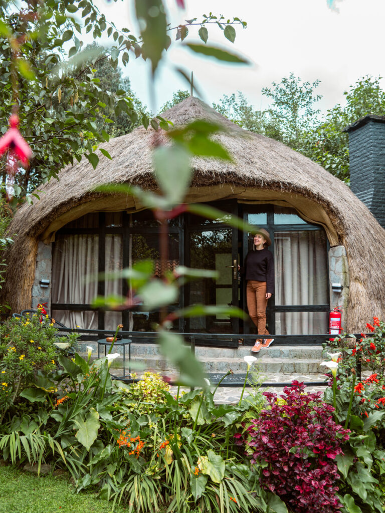 Olga stands in the doorway of a round thatched cottage surrounded by flowers at Amarembo.