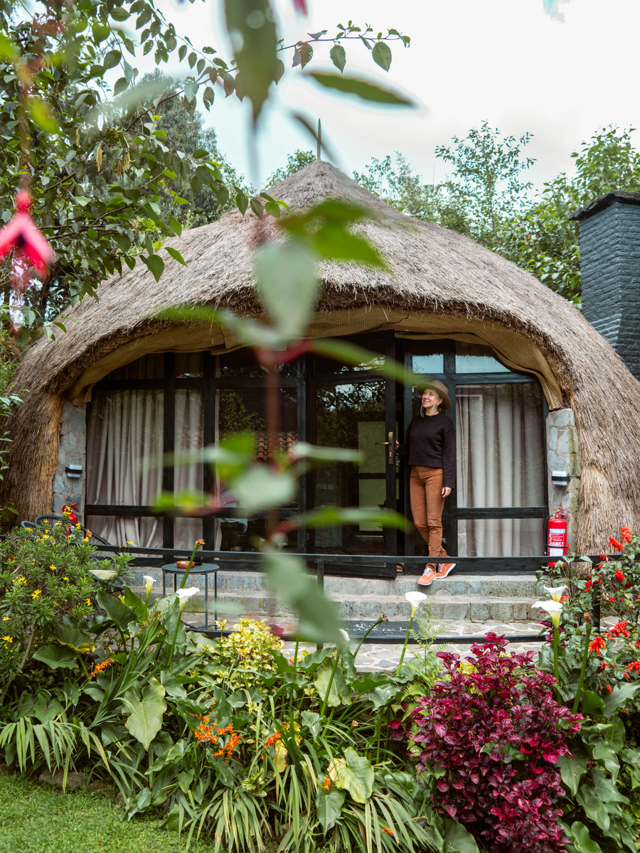 Olga stands in the doorway of a round thatched cottage surrounded by flowers at Amarembo.