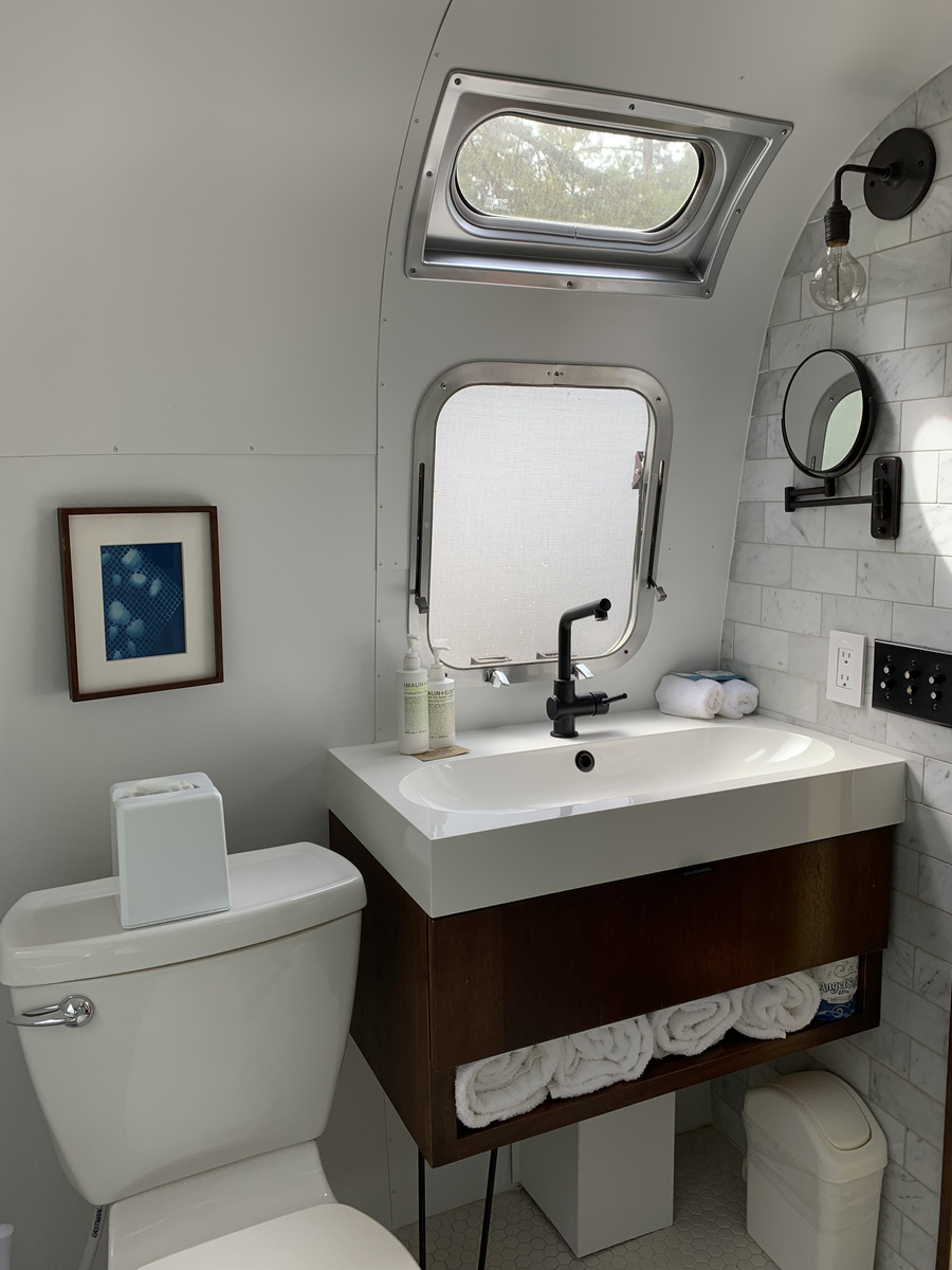 White bathroom inside an Airstream trailer with toilet, sink and a small window