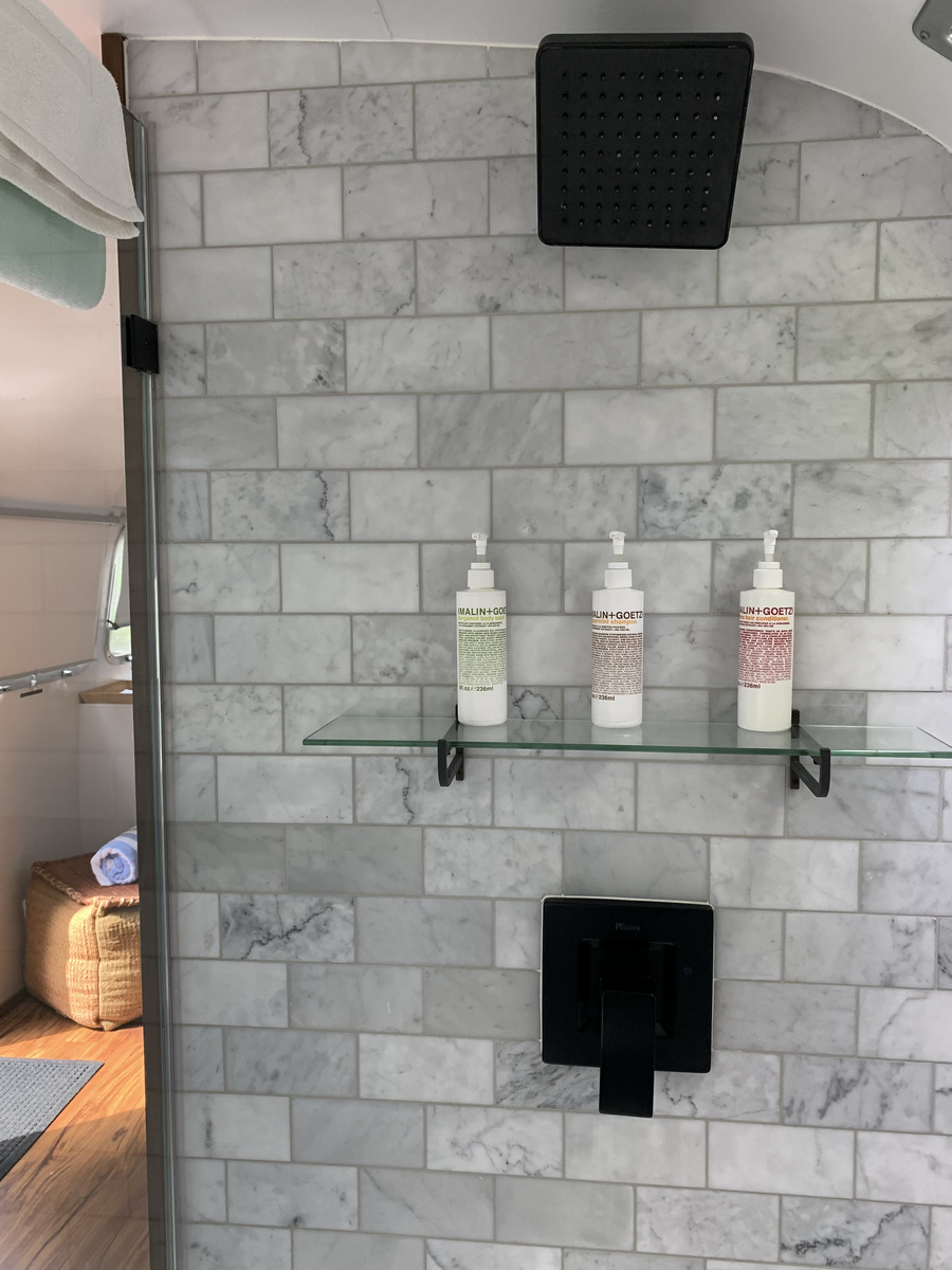 Marble-tiled Airstream shower with black fittings and three bottles of toiletries