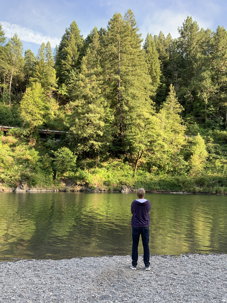 Two people standing on a stony bank beside the green Russian River