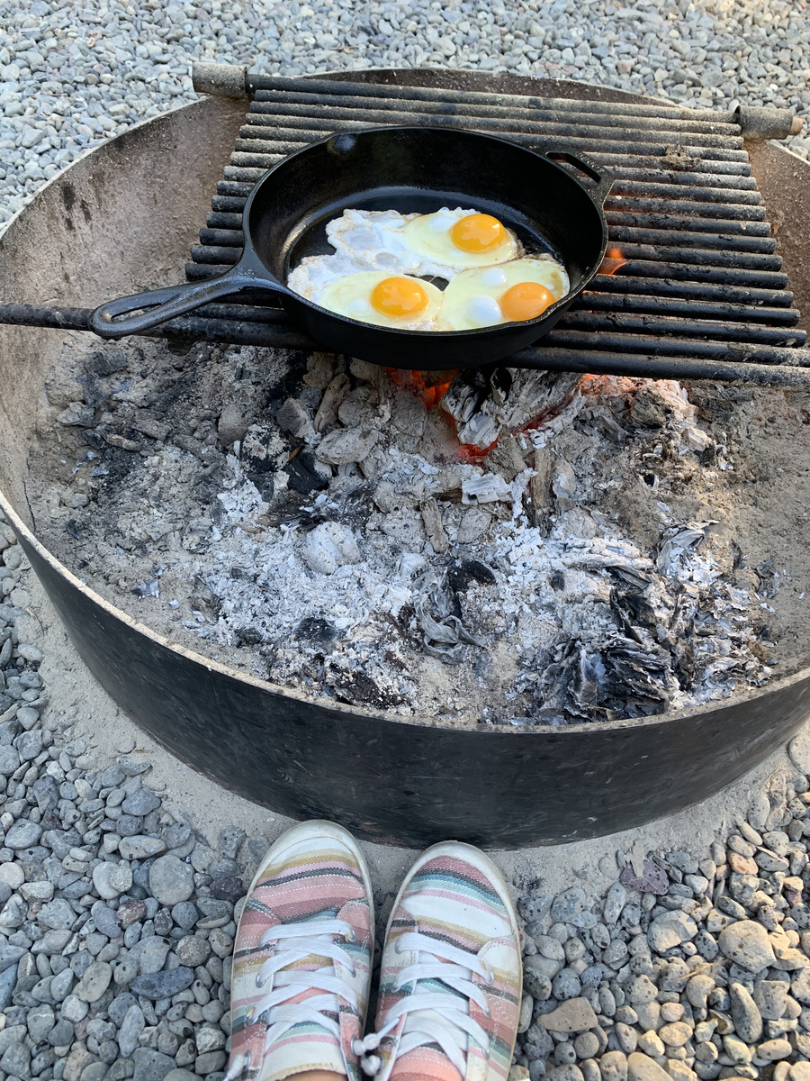 Eggs frying in a cast-iron skillet over the remains of a campfire