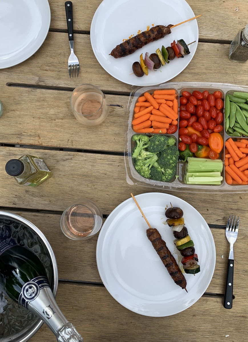 Grilled meat and vegetable skewers with bowls of vegetables on an outdoor table