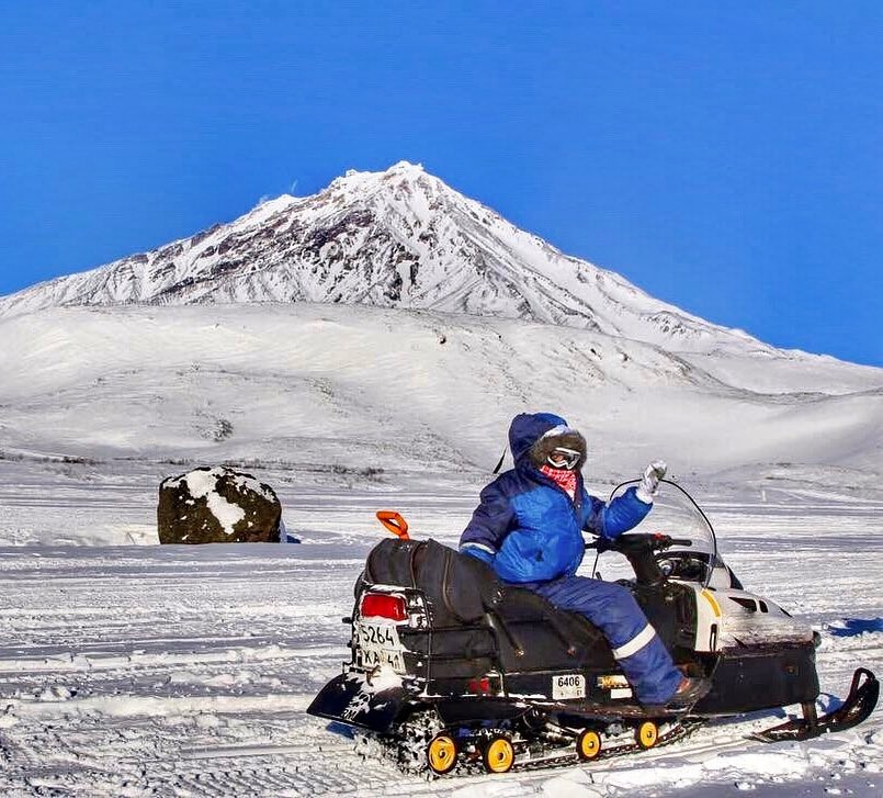 Olga sits on a snowmobile below the snow-covered Avachinsky volcano in Kamchatka