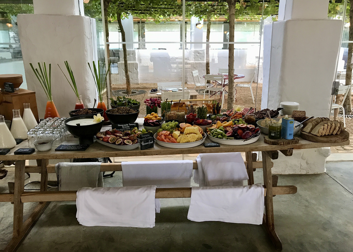 A long Babylonstoren breakfast table is covered with bread, fruit, vegetables, cheese and charcuterie.