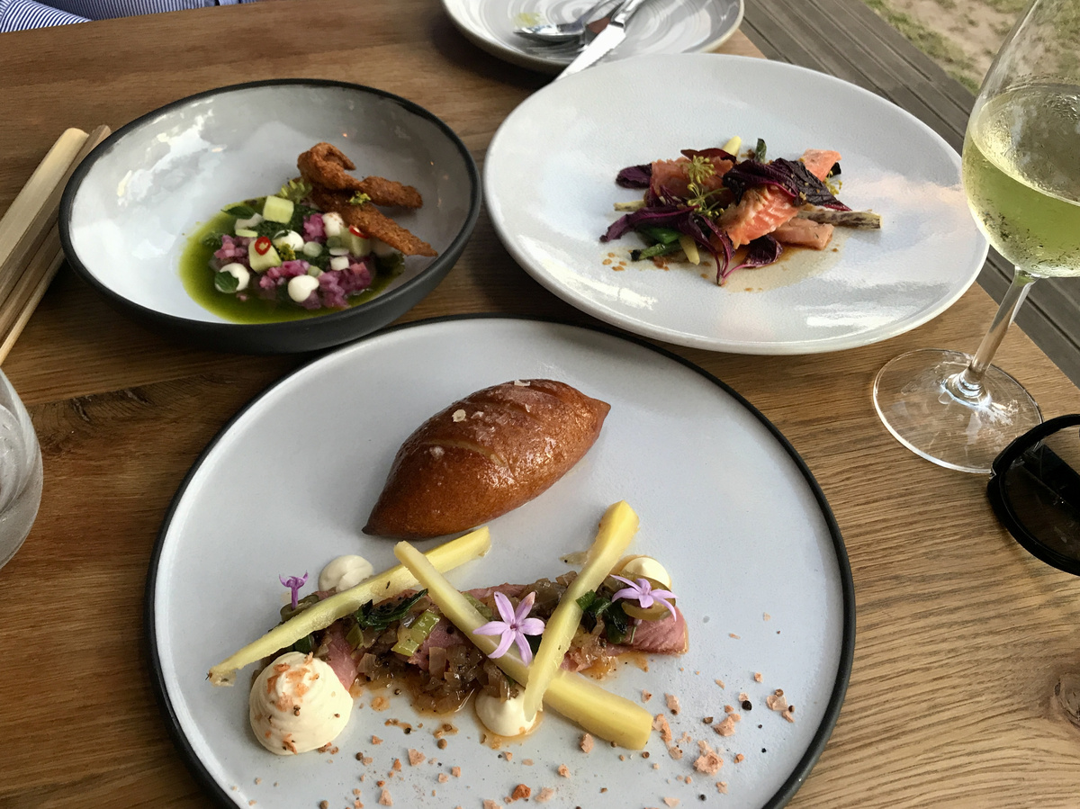 Three plated dinner courses and a glass of white wine on a wooden table at Babylonstoren.