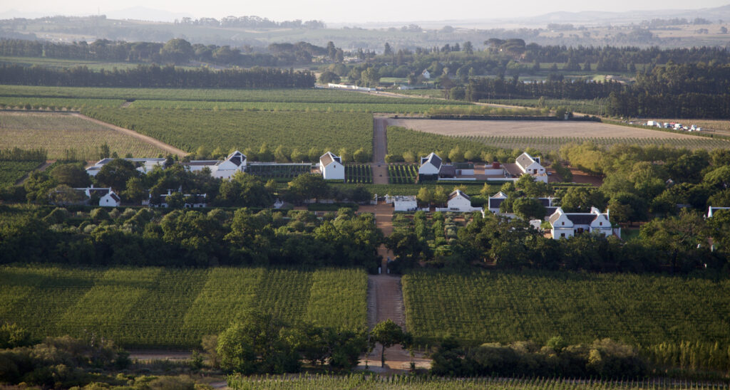 Wide aerial view of Babylonstoren farm buildings and gardens surrounded by vineyards in the Cape Winelands.
