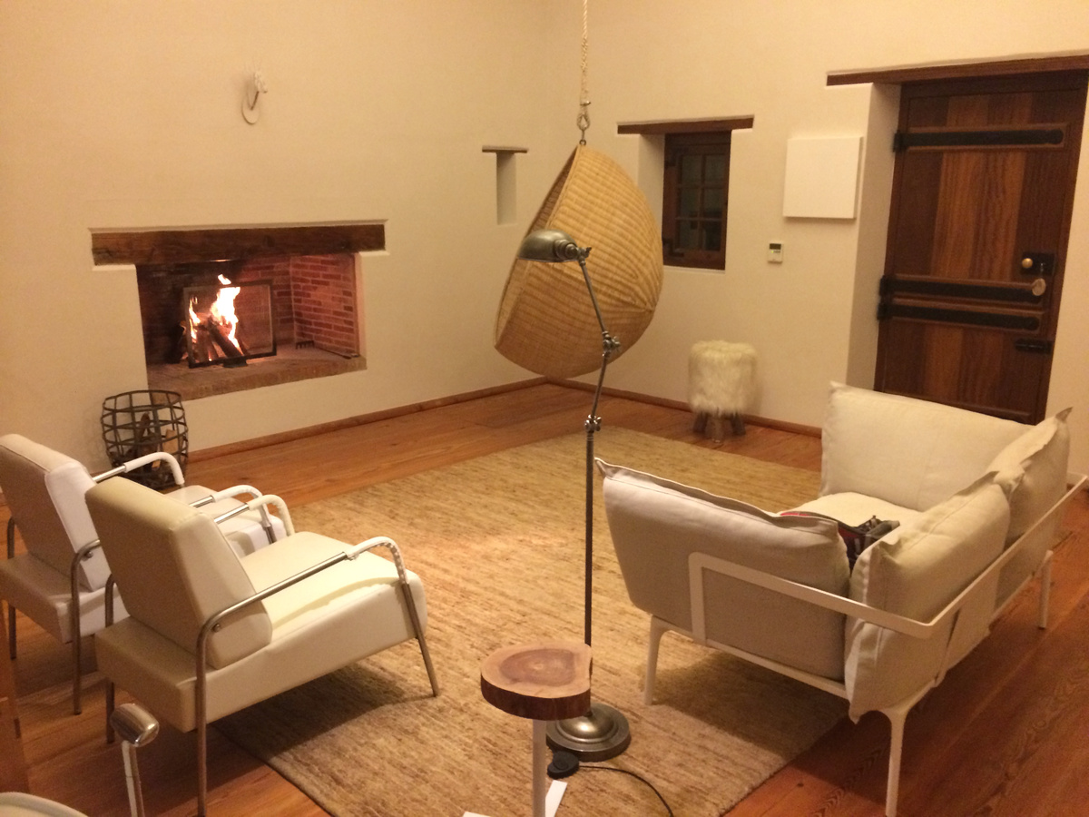 A firelit Babylonstoren sitting room with white chairs, a hanging wicker chair and wooden floors.