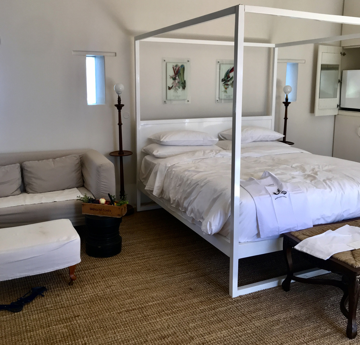 A white four-poster bed, linen sofa and wooden fruit crate in a Babylonstoren cottage room.