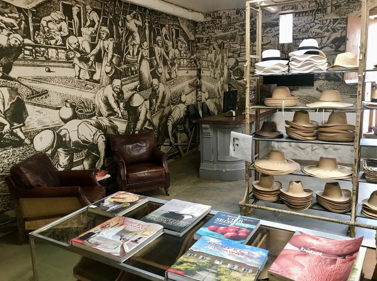 Hats, books and ceramics in a Babylonstoren shop with a black-and-white illustrated wall.