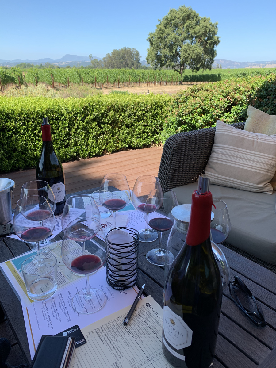 Wine bottles and tasting glasses on a terrace table overlooking vines at Benovia Winery