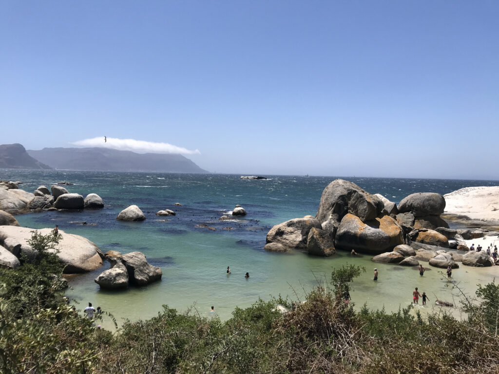 Turquoise water and rounded granite boulders enclosing the bathing cove at Boulders Beach, with mountains in the distance.