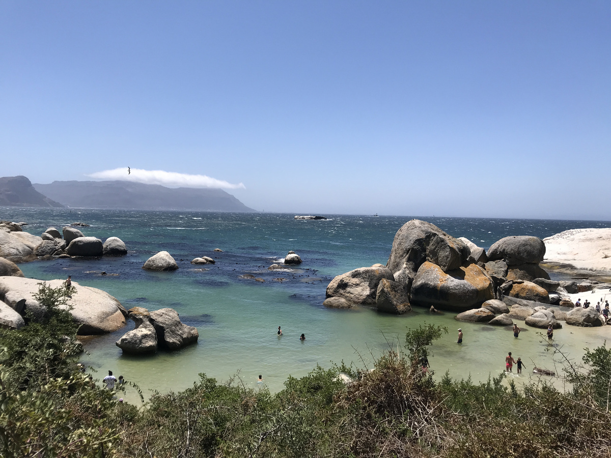 Turquoise water and rounded granite boulders enclosing the bathing cove at Boulders Beach, with mountains in the distance.