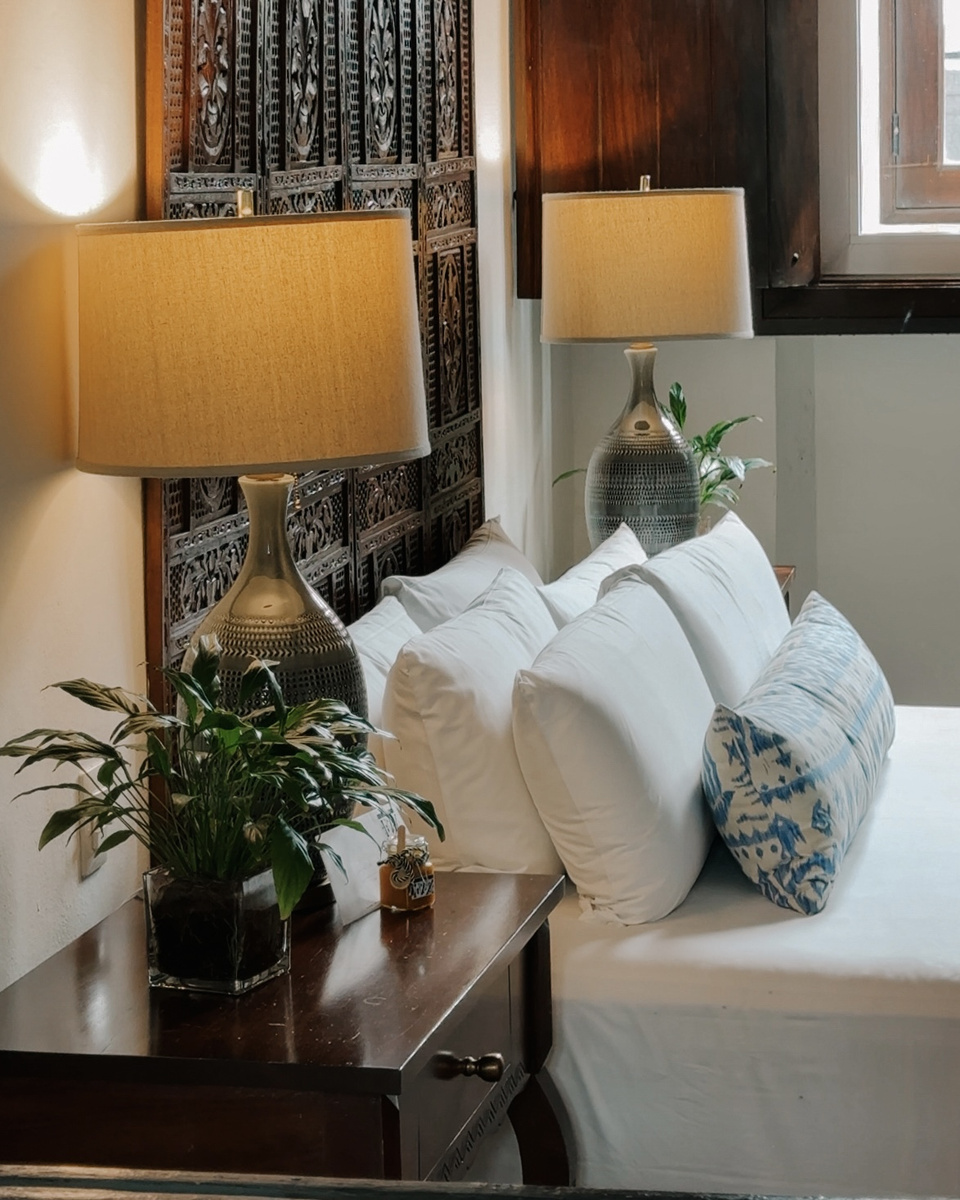 A bedside table and ceramic lamps stand beside the carved headboard in a Casa del Pozo guest room at Casas del XVI.