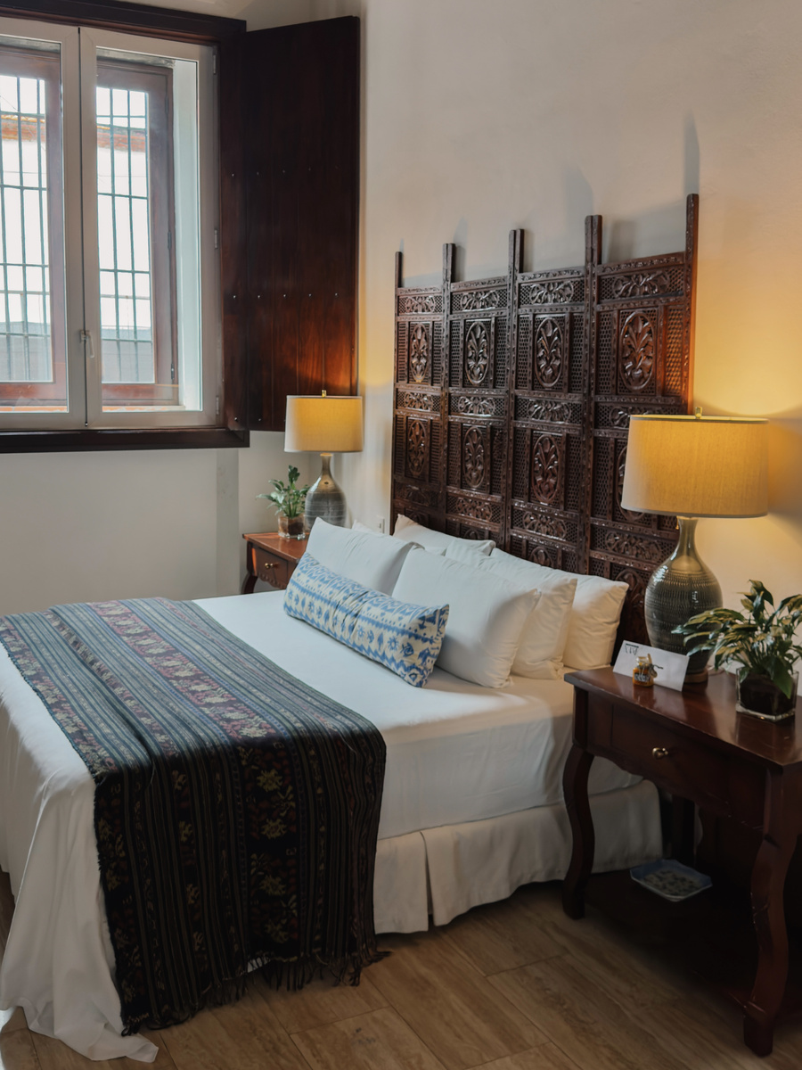 A Casa del Pozo guest room has a carved dark-wood headboard, blue-and-white textiles and shuttered windows.