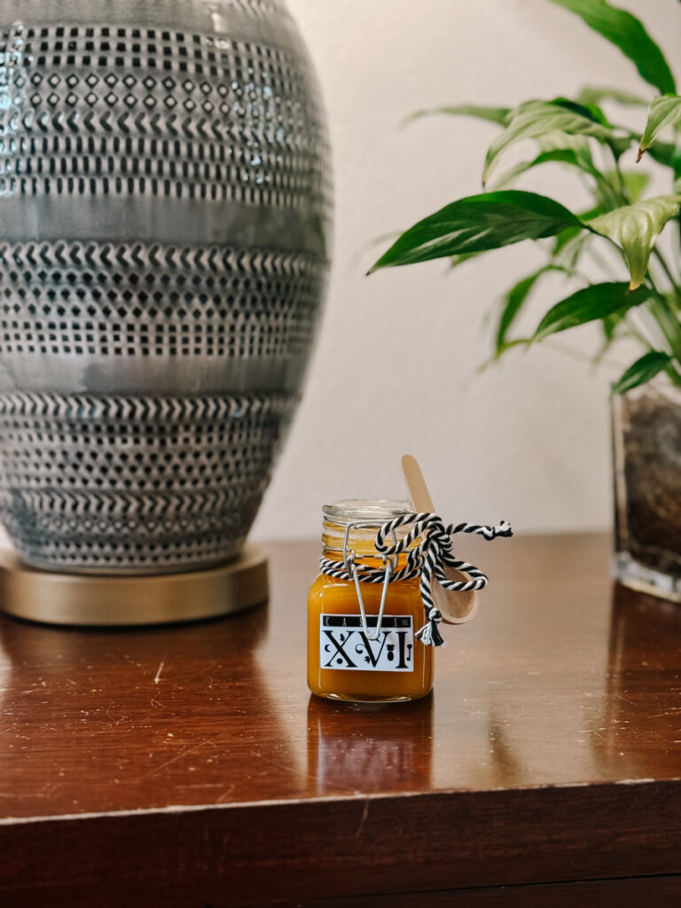 A tiny jar of marmalade with a Casas del XVI label sits beside a ceramic vessel and a green plant.