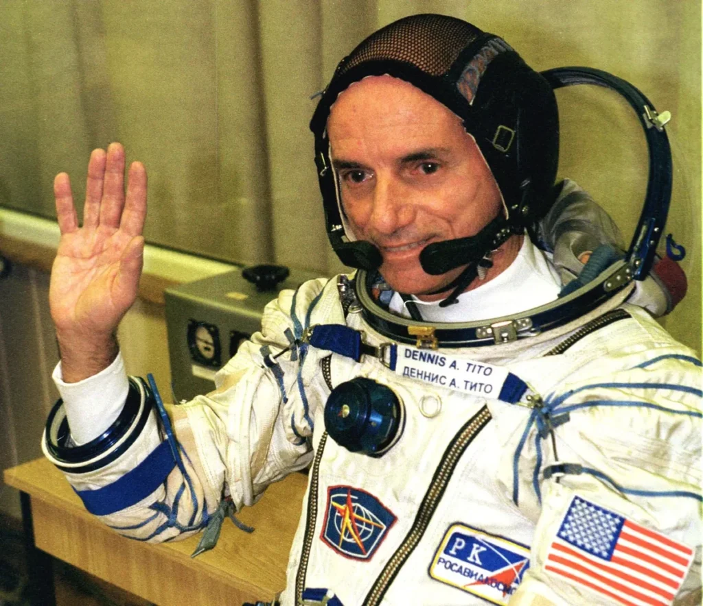 Dennis Tito waves in a white Sokol pressure suit and black communications cap before his 2001 Soyuz launch.