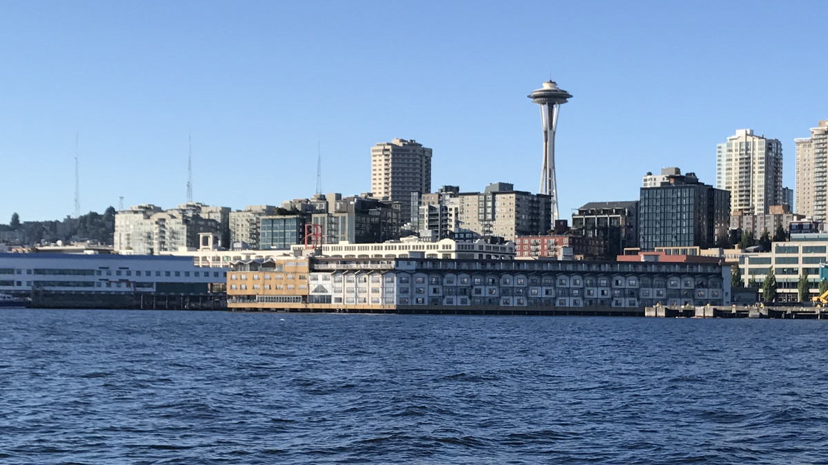 The Edgewater Hotel stretches across Pier 67 beneath its red neon sign and the Space Needle, seen from Elliott Bay.