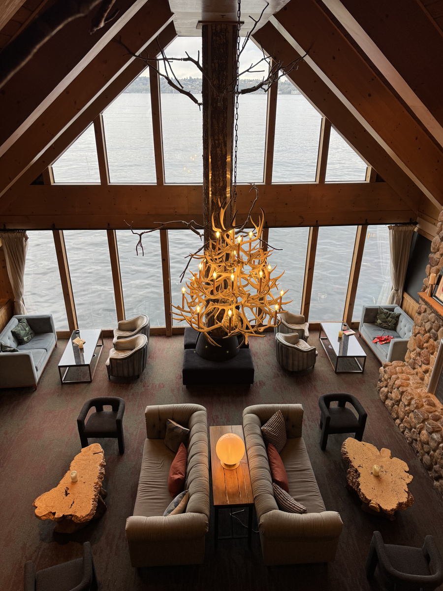 The Edgewater Hotel lobby seen from above, with an antler chandelier, timber roof, river-stone wall and Elliott Bay windows.