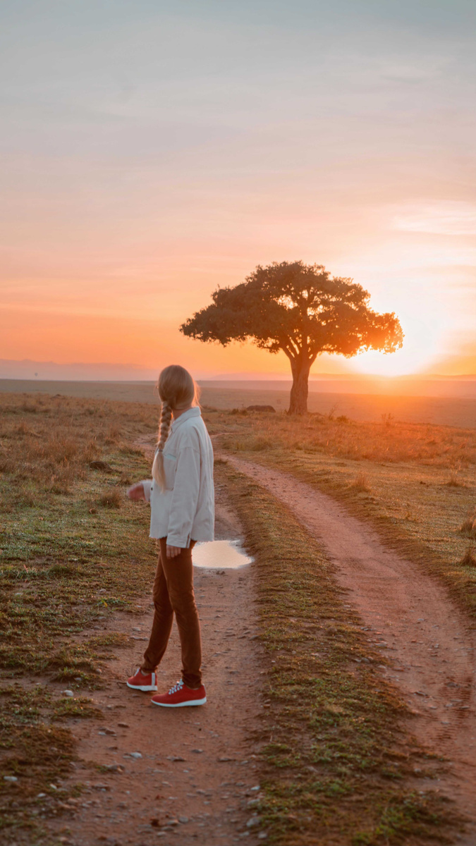 Olga standing on a Masai Mara track beside an acacia tree at sunset.