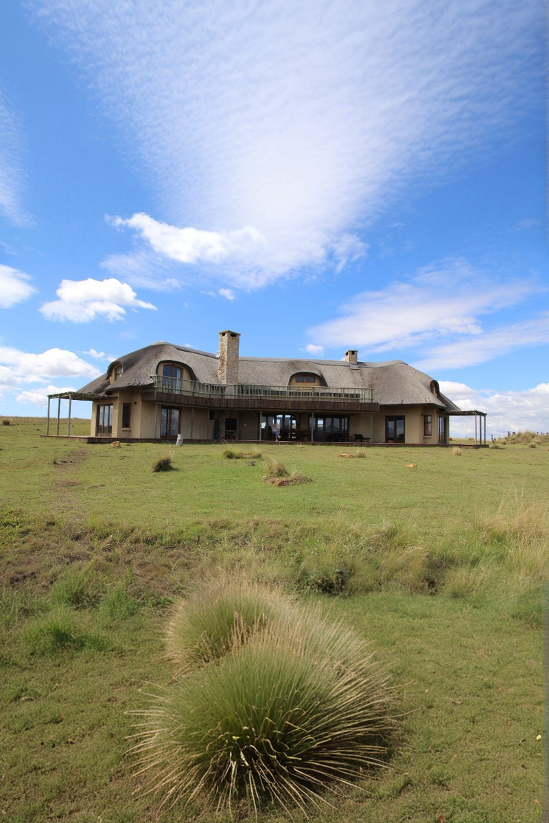 Thatched Gondwana villa on a green hillside beneath a broad cloudy sky