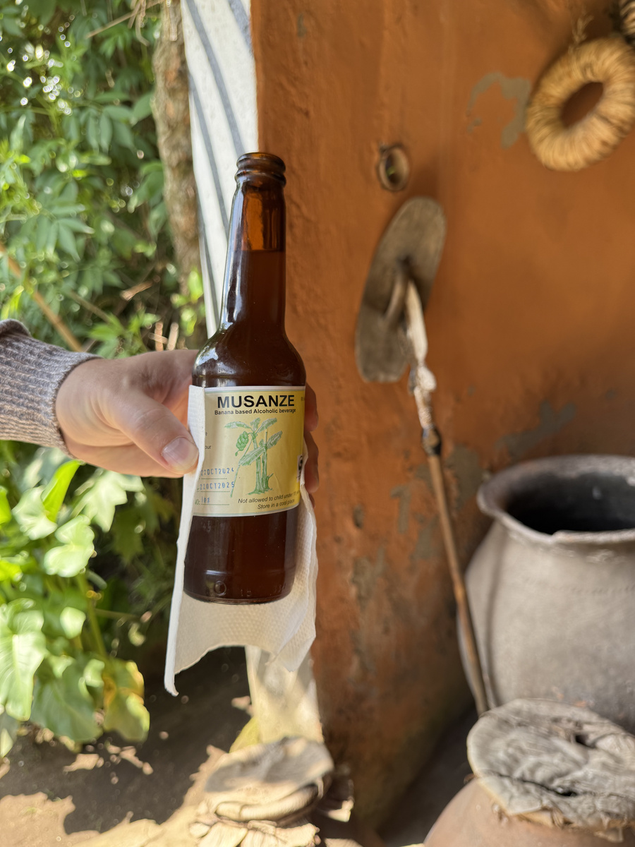 A hand holds a bottle during a banana-beer demonstration beside a clay pot at Gorilla Guardians Village.