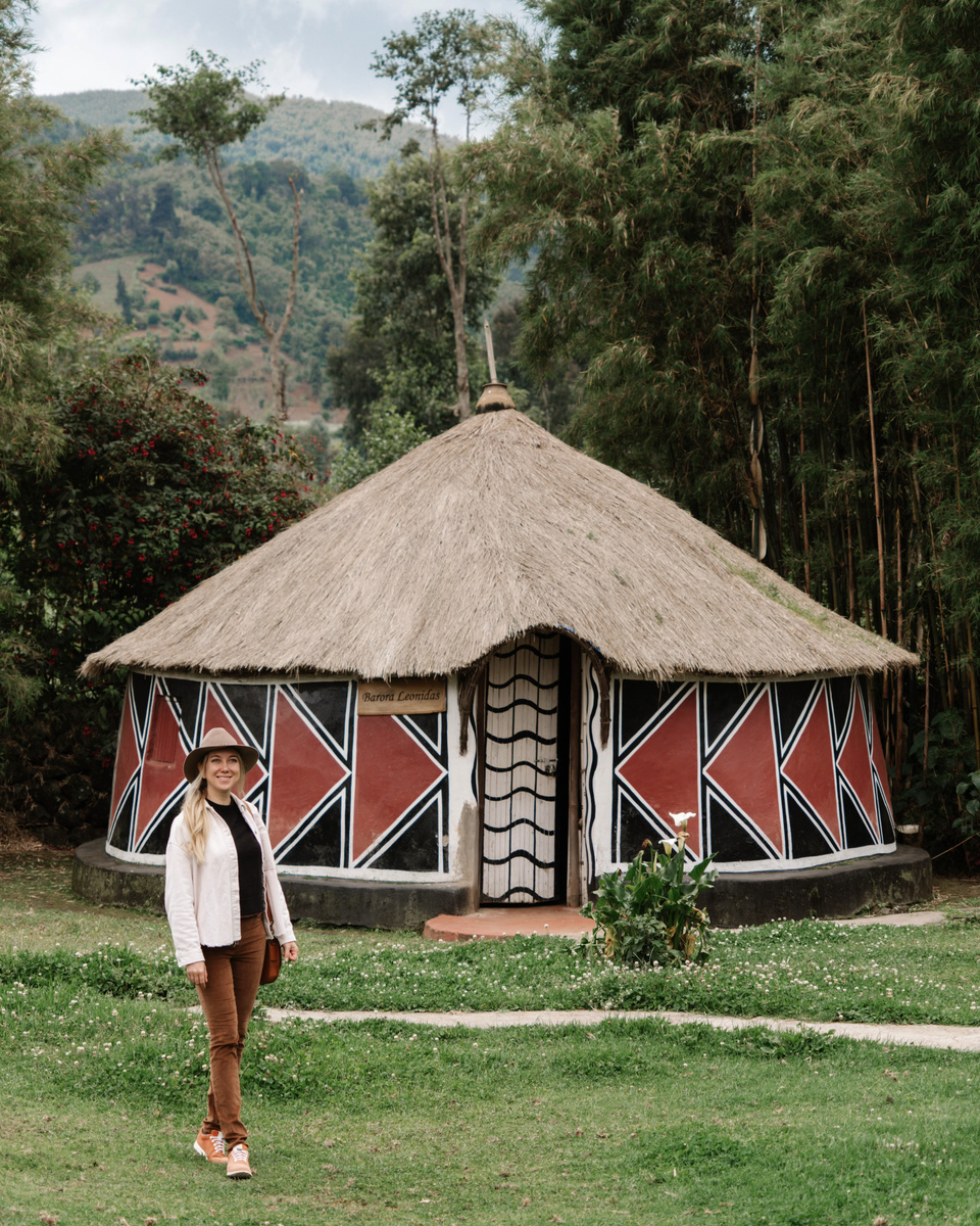 Olga stands before a round painted and thatched building at Gorilla Guardians Village.
