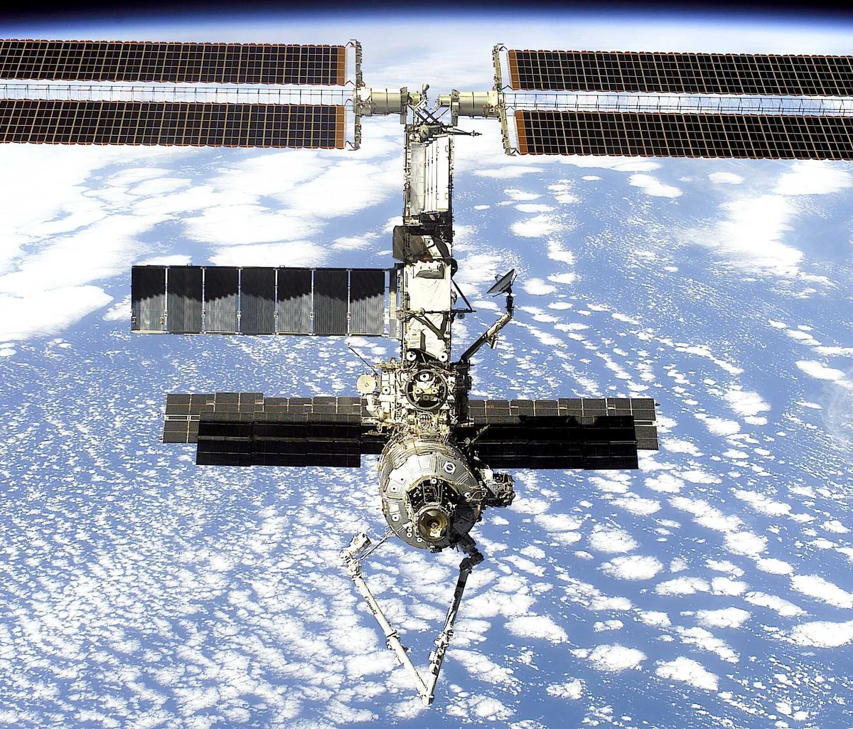 The International Space Station above Earth in April 2001, its long rectangular solar arrays extending from a compact central structure.