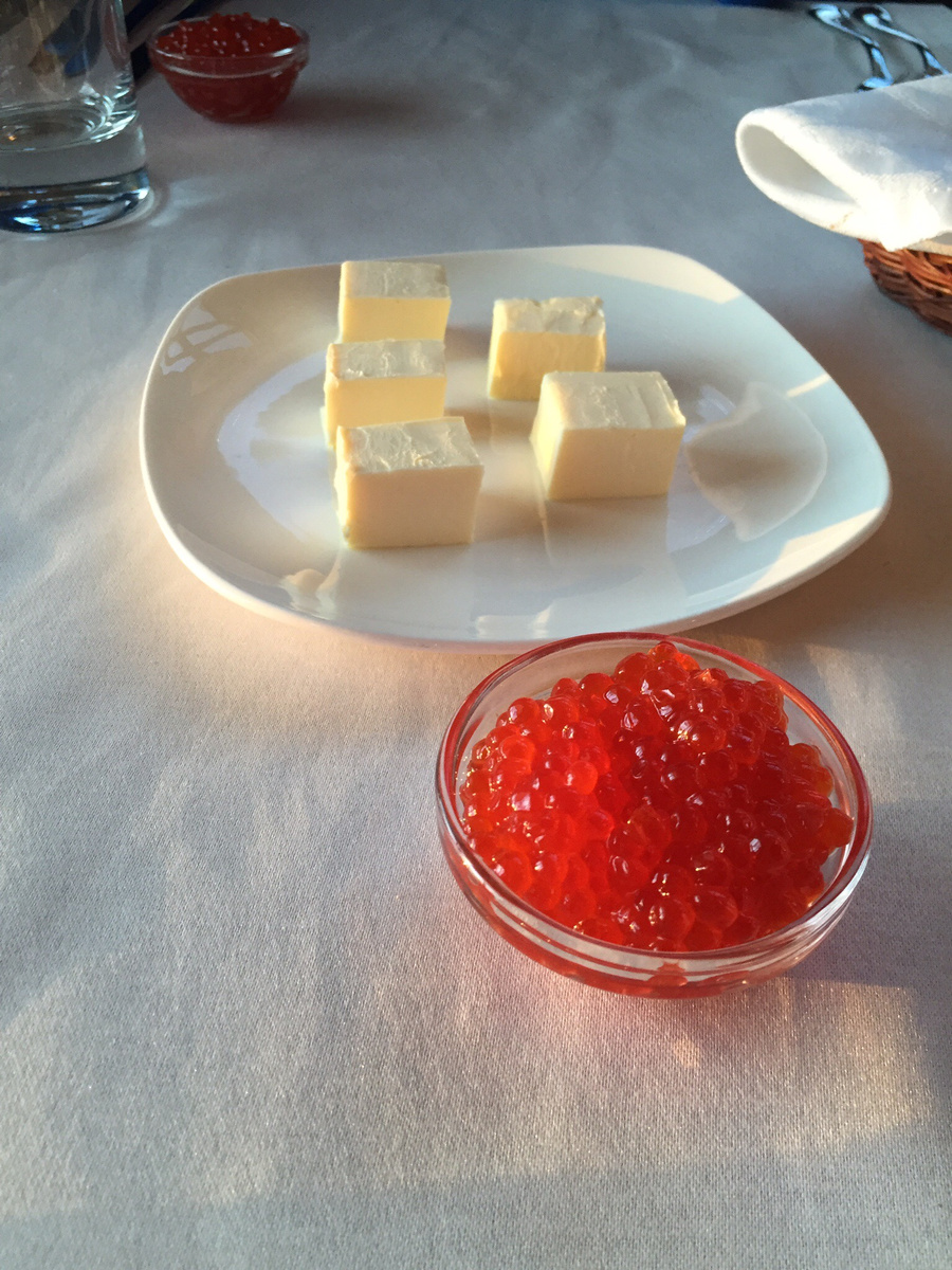 A glass bowl of red Kamchatka caviar served beside large cubes of butter at breakfast
