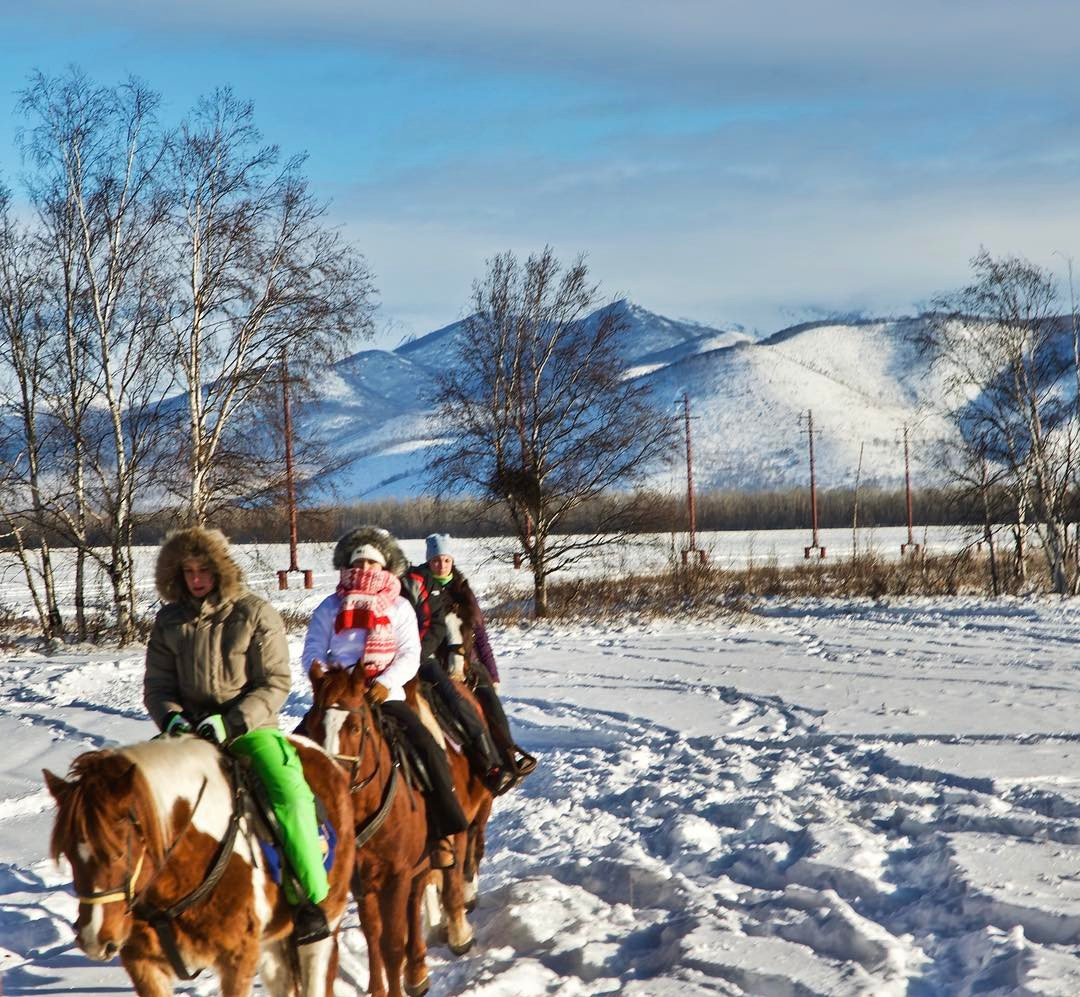 Three riders cross a snowy Kamchatka landscape on horseback with mountains behind them