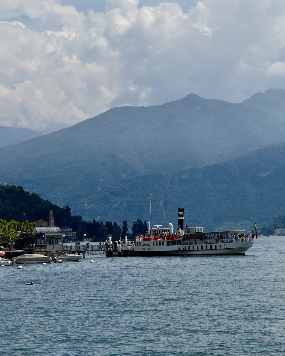 The historic passenger ferry Concordia docks at Lenno on Lake Como beneath cloud-covered mountains.