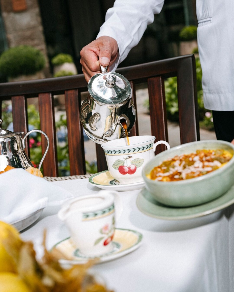 A server pours coffee from a polished silver pot into patterned china at breakfast in Oqre.