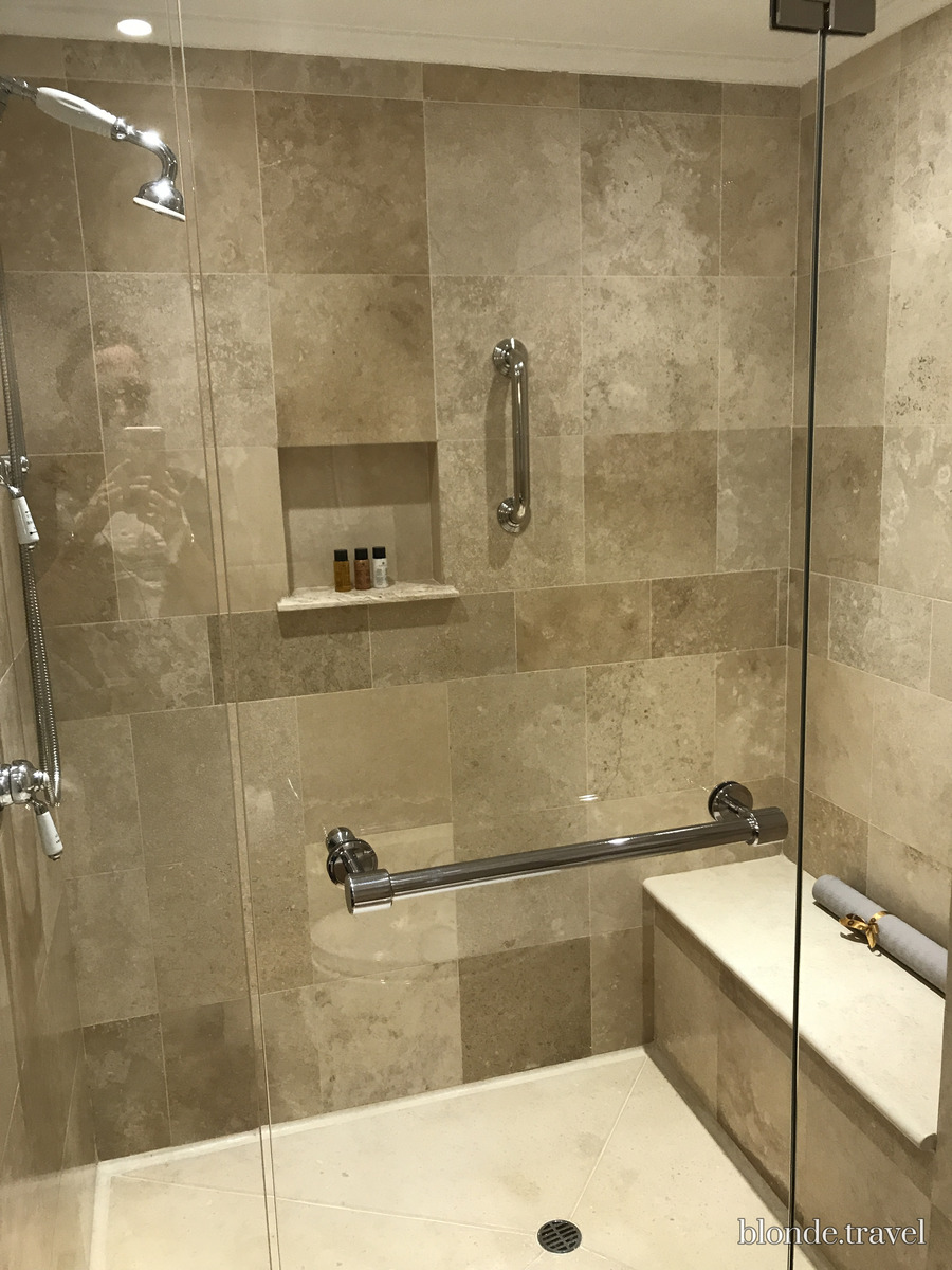 A stone-lined walk-in shower with glass enclosure and chrome fittings in Olga's Monasterio room.