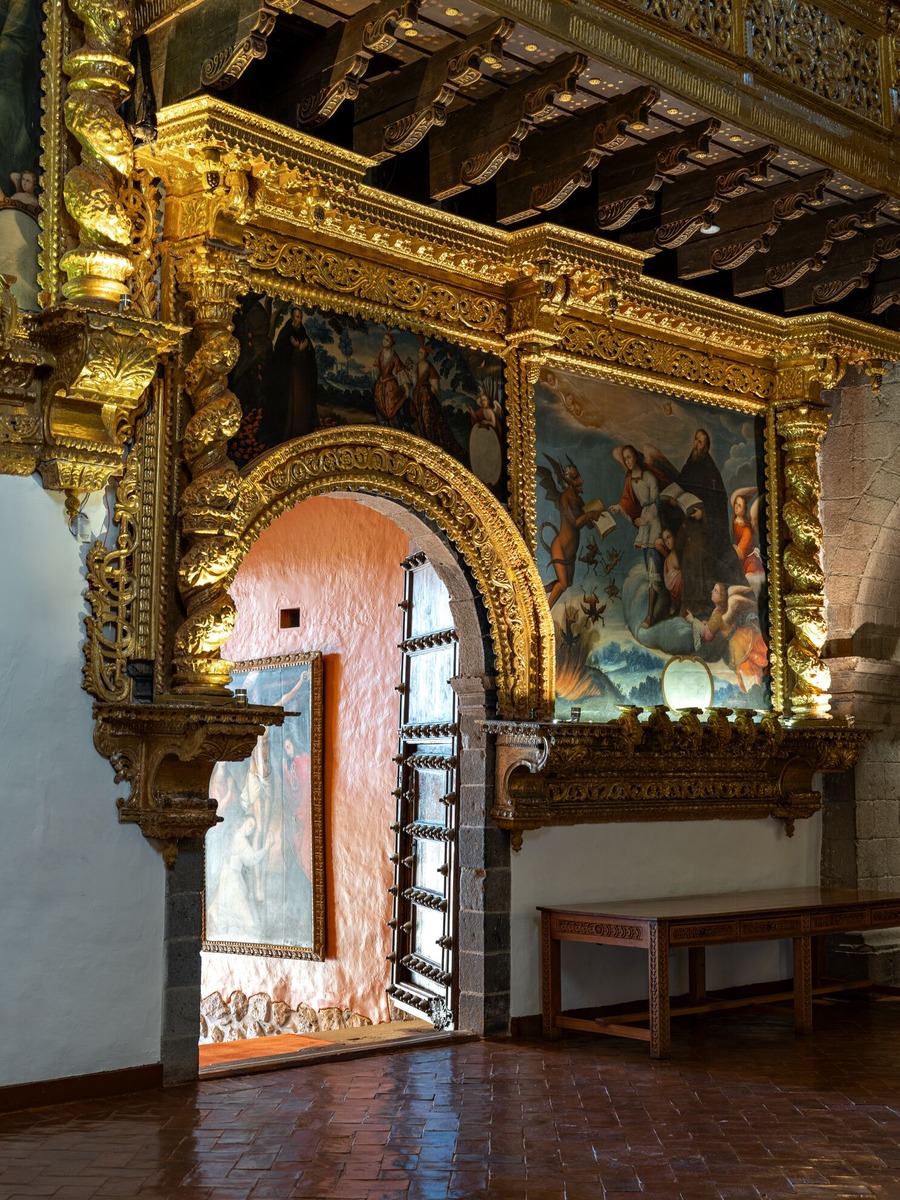 Gilded carved wood and religious paintings frame a stone arch inside Monasterio's San Antonio de Abad Chapel.