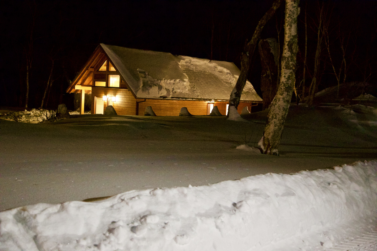 An illuminated wooden cottage at North Adventures Kamchatka surrounded by snow at night