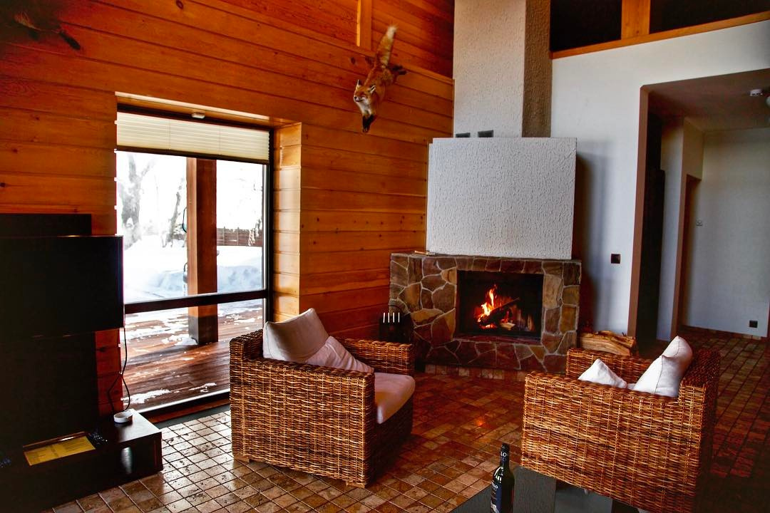 Wood-paneled North Adventures cottage living room with wicker chairs and a real stone fireplace burning