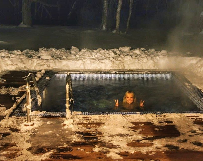 Olga in a steaming private outdoor thermal pool surrounded by snow at night in Kamchatka