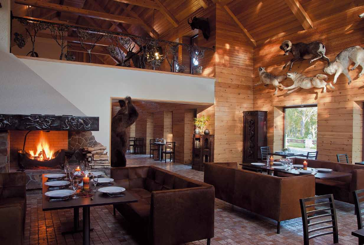 Wooden dining room at North Adventures Kamchatka, with a stone fireplace, set tables and mounted animals