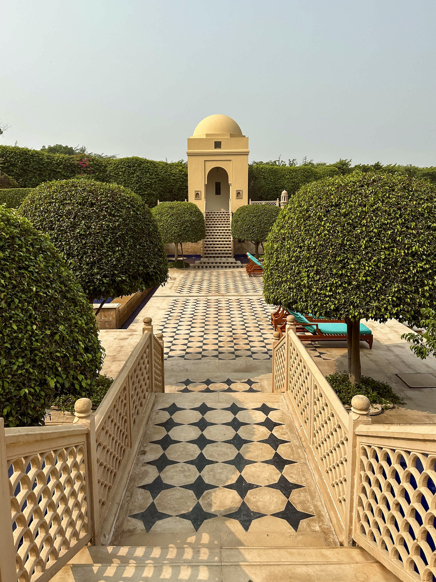 A black-and-white stone walkway runs between clipped trees toward a domed pavilion at The Oberoi Amarvilas.