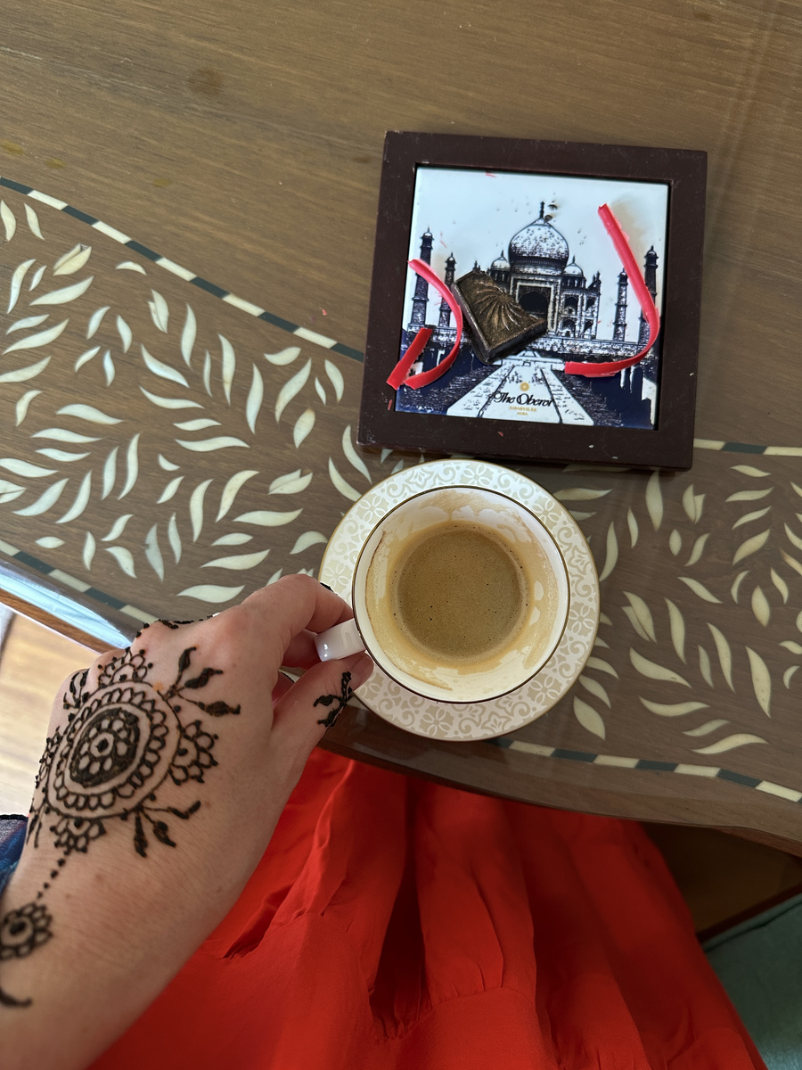 Olga's fresh floral mehendi beside a cup of coffee and an Oberoi chocolate decorated with the Taj Mahal.