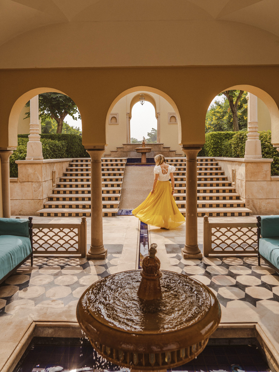 Olga in a yellow skirt crosses a fountain courtyard framed by arches at The Oberoi Amarvilas.